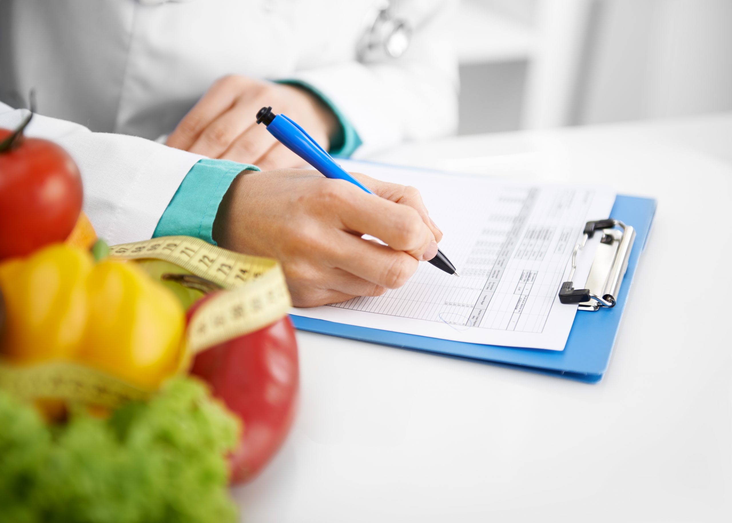 Doctor nutritionist writing case history in the office. Young woman dietitian prescribing recipe.