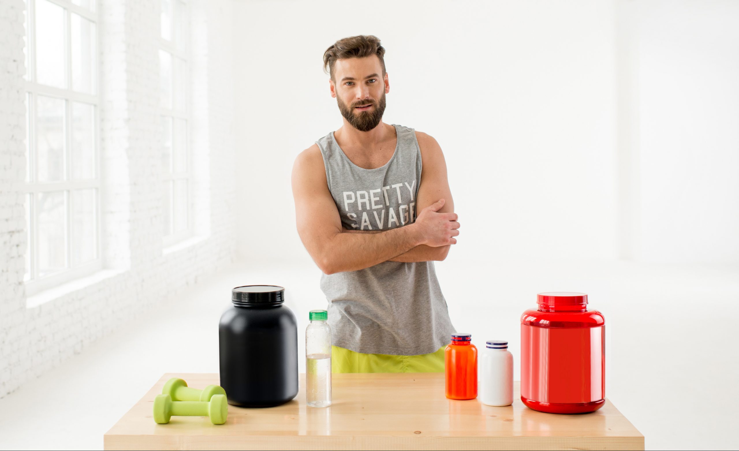Portrait of athletic man in sportswear with proteins and vitamins in the white gym interior